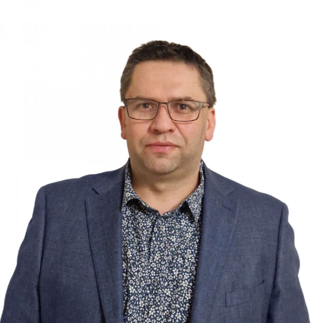 Mężczyzna w okularach, ubrany w niebieską marynarkę i koszulę w kwiaty, stoi na neutralnym tle.