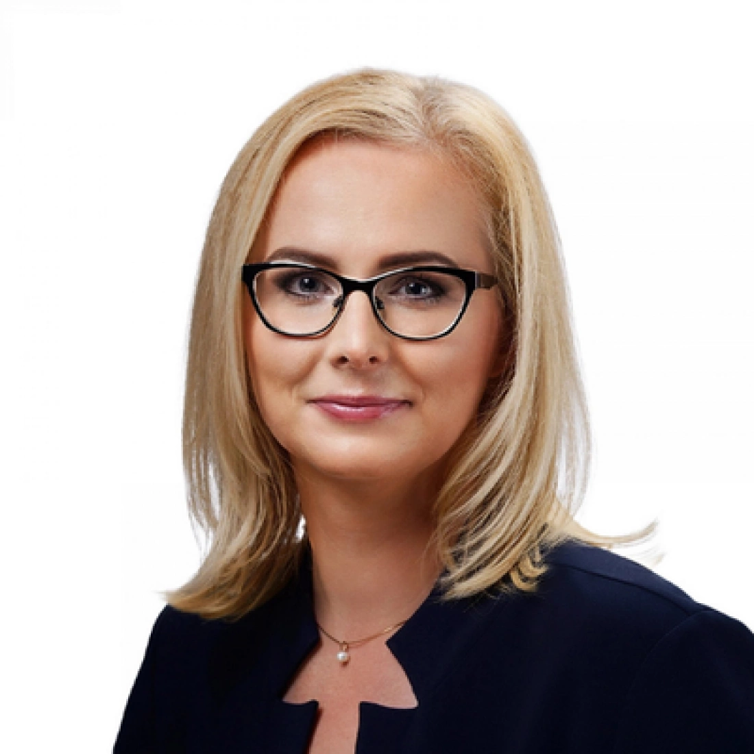 Kobieta z blond włosami, w okularach, uśmiecha się. Ma na sobie ciemny strój. Tło jasne.