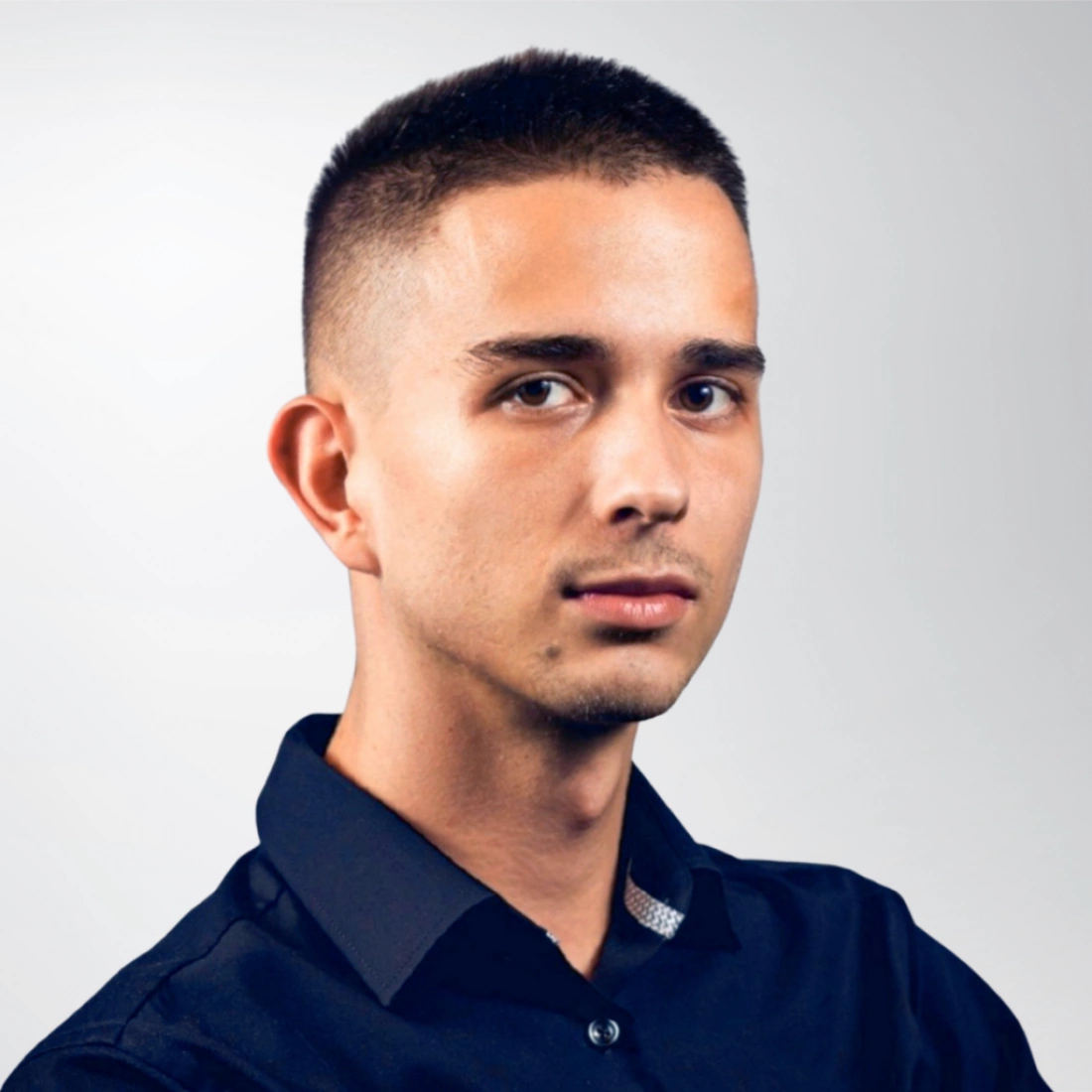 Młody mężczyzna w czarnej koszuli, patrzący poważnie w stronę kamery.