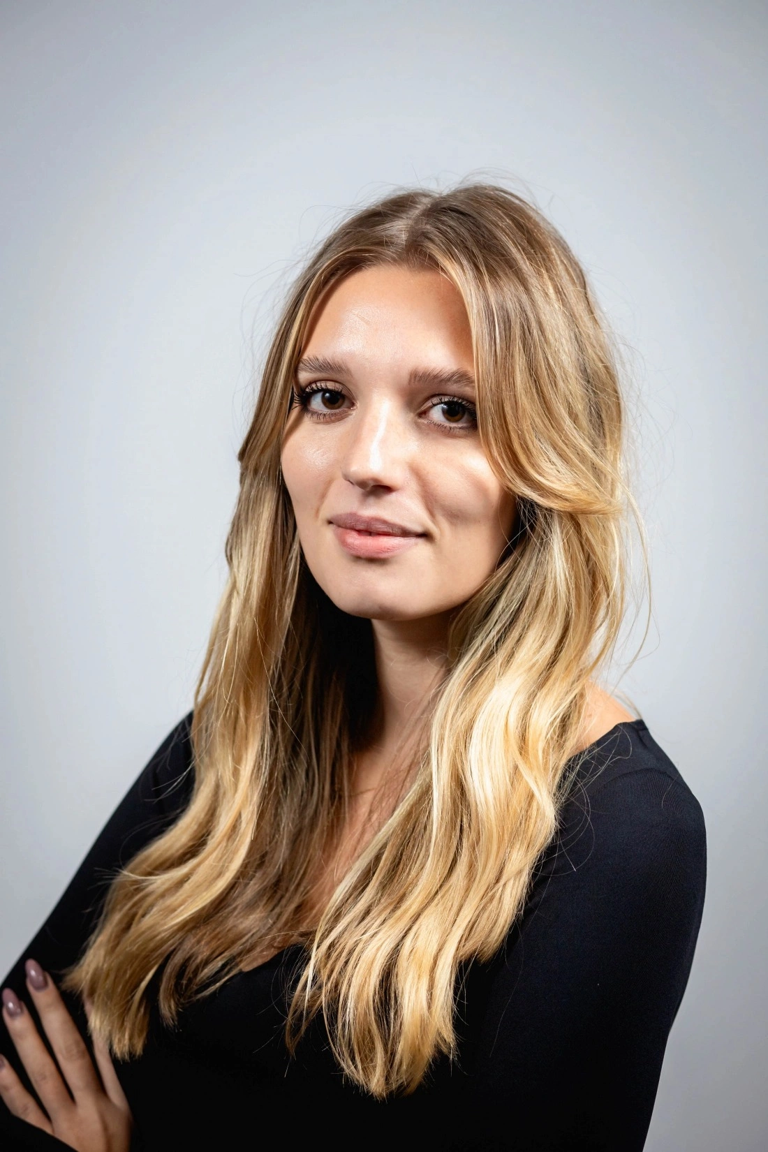 Portret młodej kobiety z długimi, falującymi włosami, ubranej w czarną bluzkę, z pewnym wyrazem twarzy. Tło jasne.
