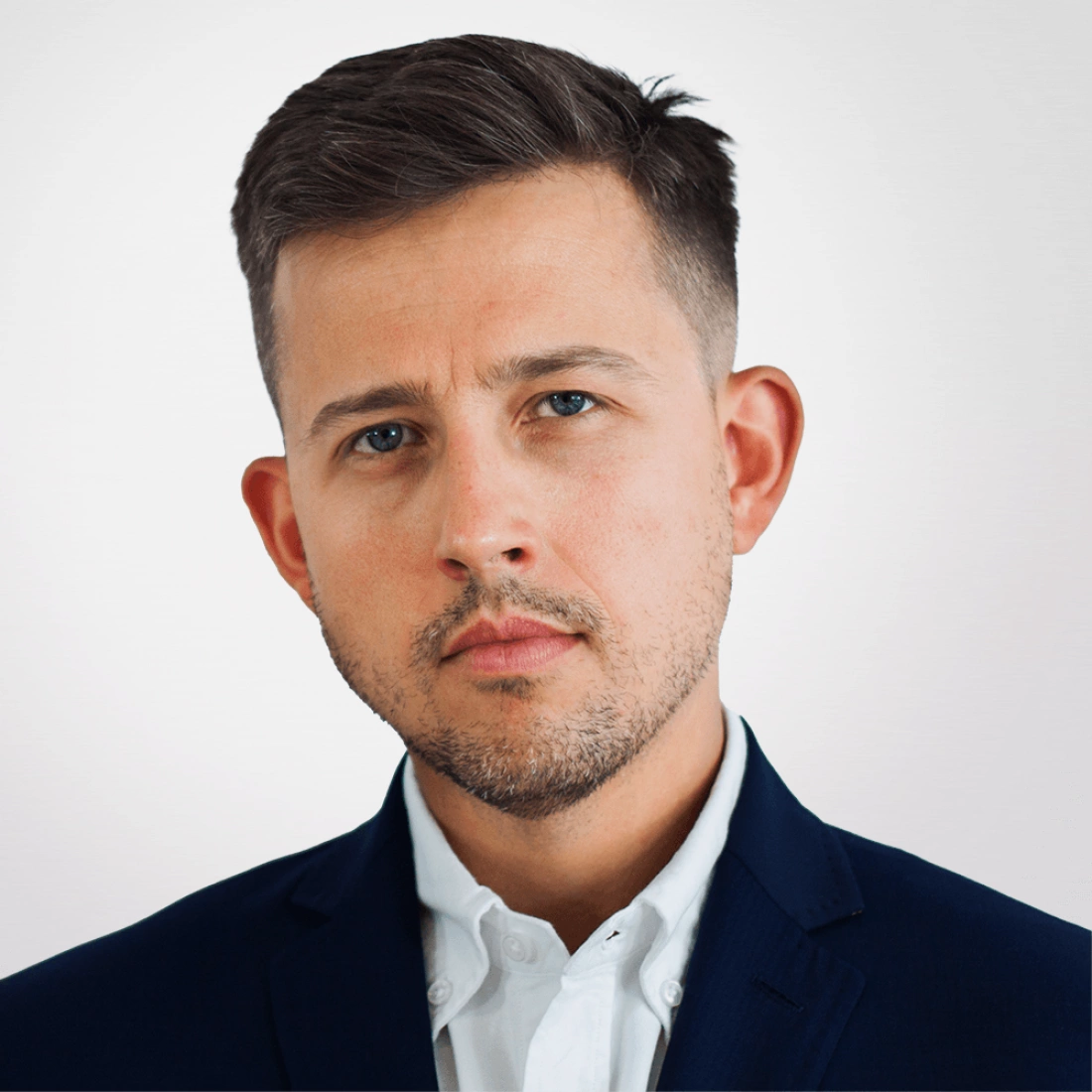 Mężczyzna w eleganckim garniturze, z poważnym wyrazem twarzy, patrzy bezpośrednio w obiektyw.