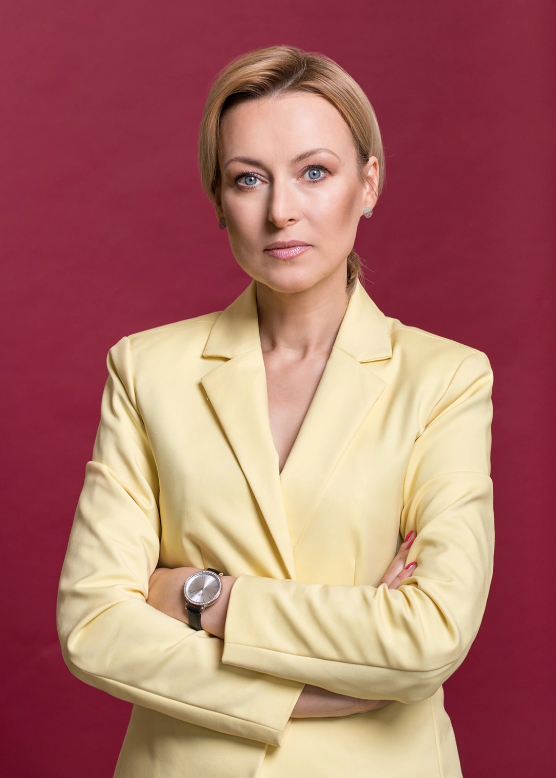 Mężczyzna w niebieskim garniturze z pomarańczowym krawatem, stoi z założonymi rękami.